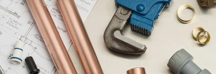 Rohrleitungen, Fittings und eine Rohrzange auf einem Bauplan.